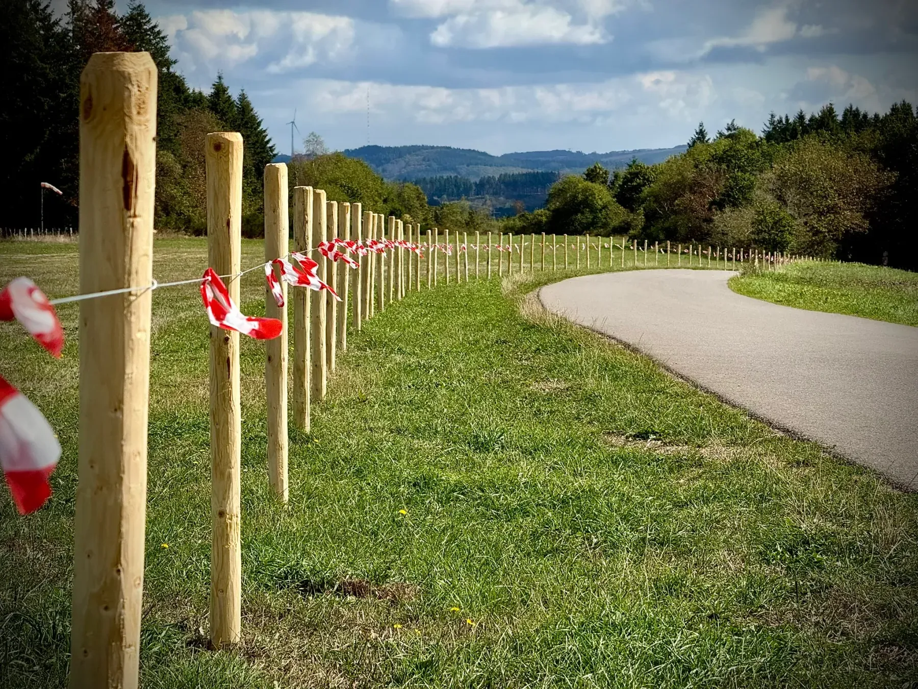Wooden posts strung with red-and-white barrier tape, marking the edge of the work area alongside the paved path