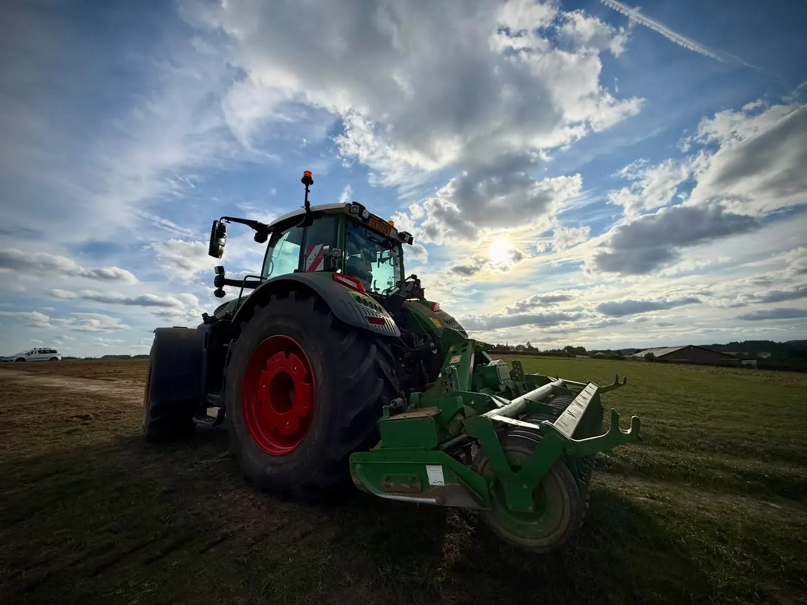 A tractor with a mounted implement standing at the edge of the field in the low evening sun